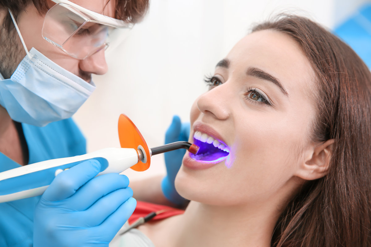 Dentist doing procedure with dental curing UV light in clinic