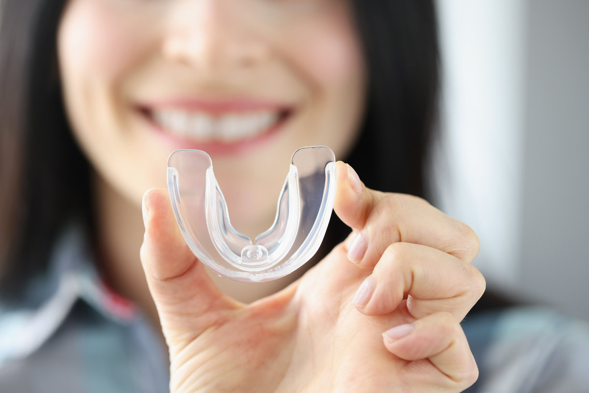Smiling woman holds transparent plastic mouth guard in her hand. Correction of malocclusion and bruxism concept