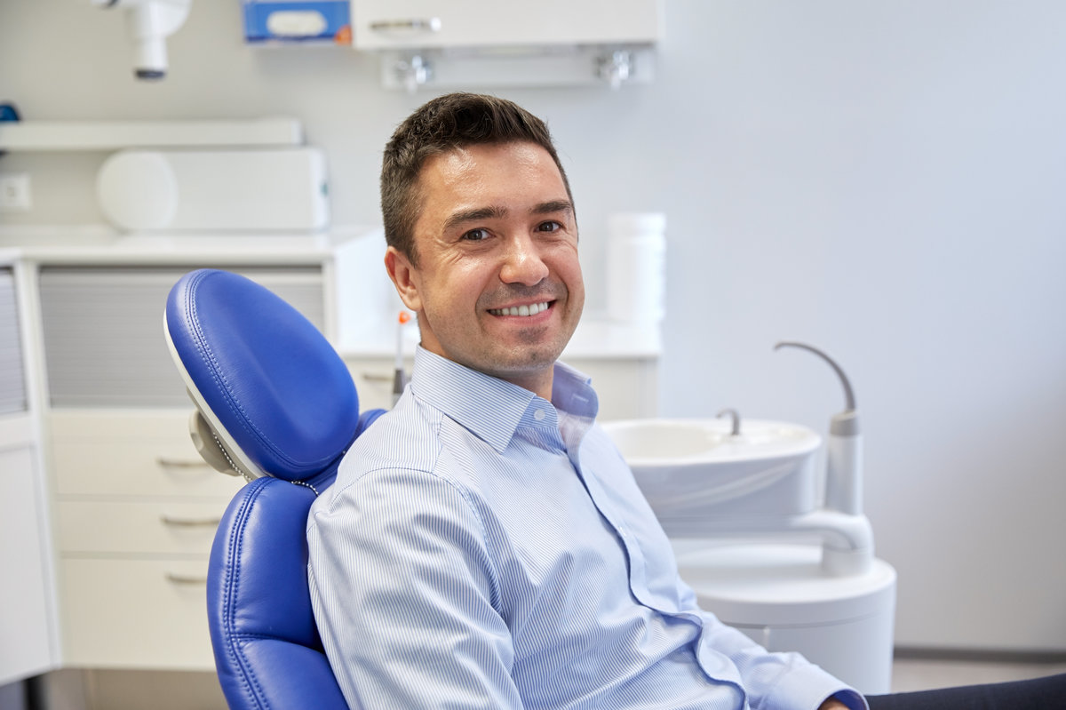 people, medicine, stomatology and health care concept - happy male patient sitting on dental chair at clinic office