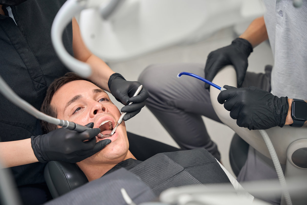 Experienced woman dentist drilling male client tooth to remove caries and clean the fissures, professional caries treatment, painless oral care
