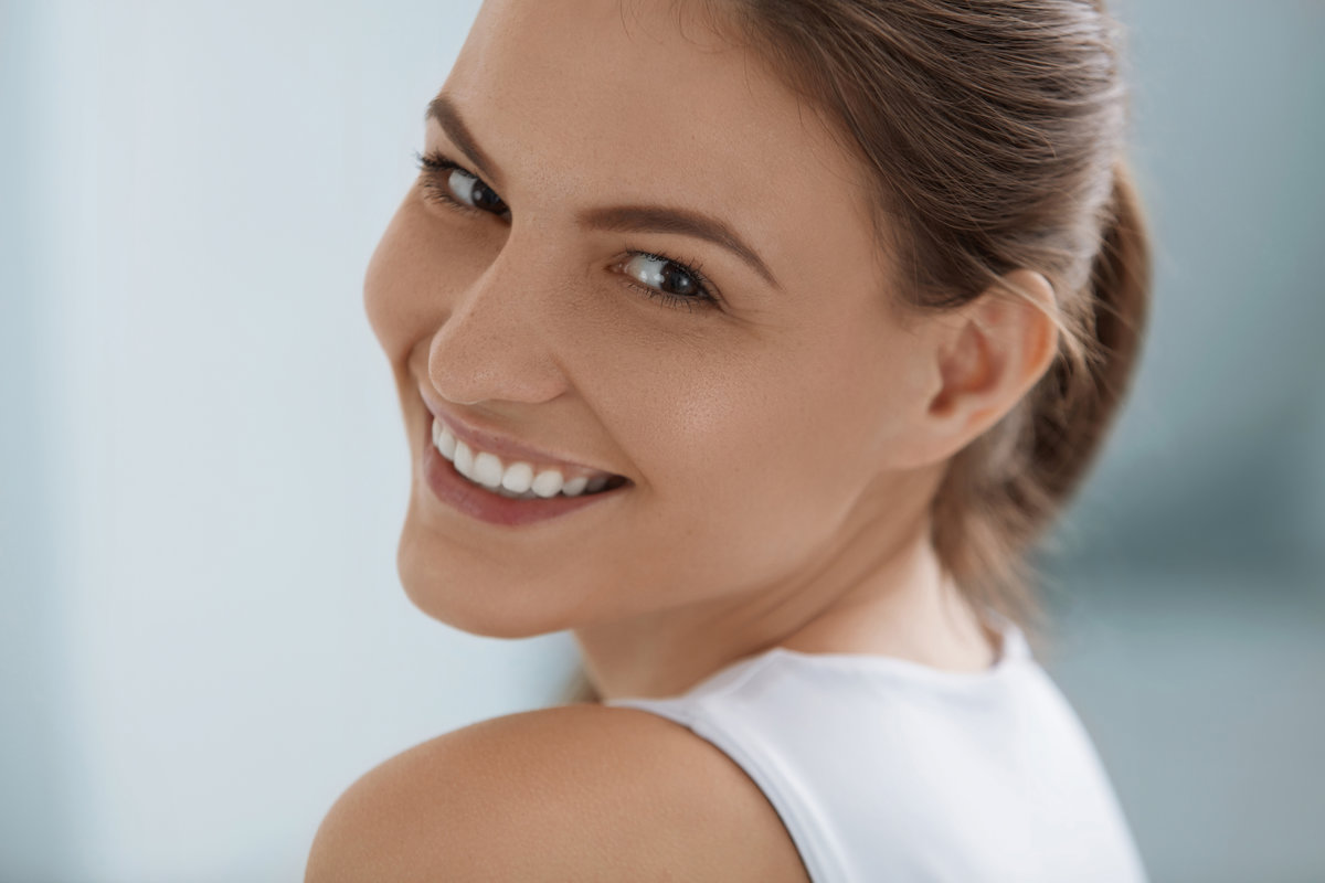 Smiling woman face with white teeth, smile, clean skin and natural makeup closeup portrait on light background