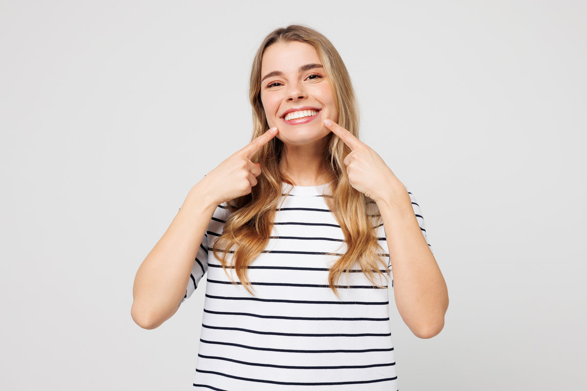 Young happy smiling Caucasian cheerful woman wear striped t-shirt casual clothes point index fingers on opened mouth teeth isolated on plain solid white background studio portrait. Lifestyle concept